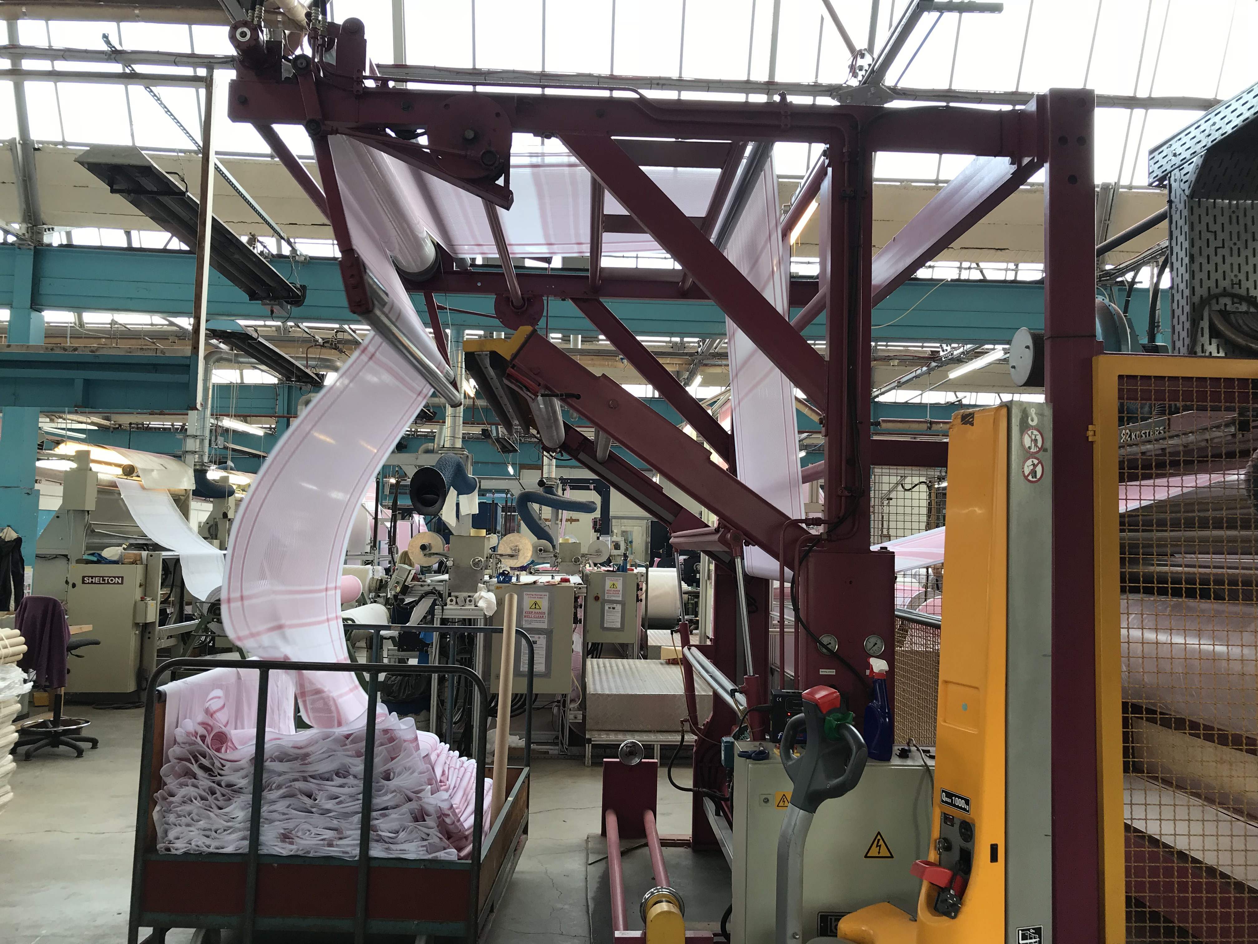 Industrial machinery guiding fabric through overhead rollers on a factory floor