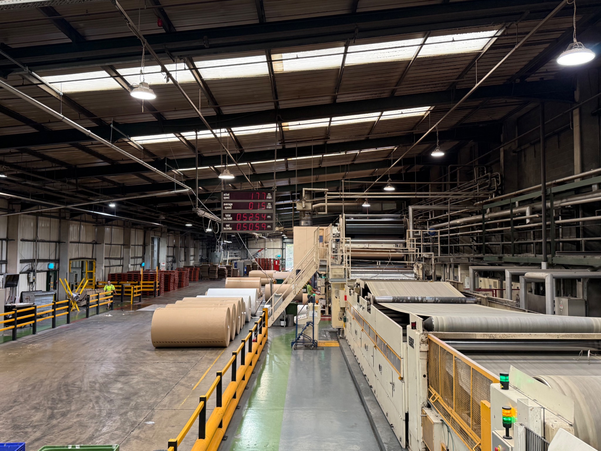 Corrugated board production line with paper reels feeding a continuous web through industrial rollers